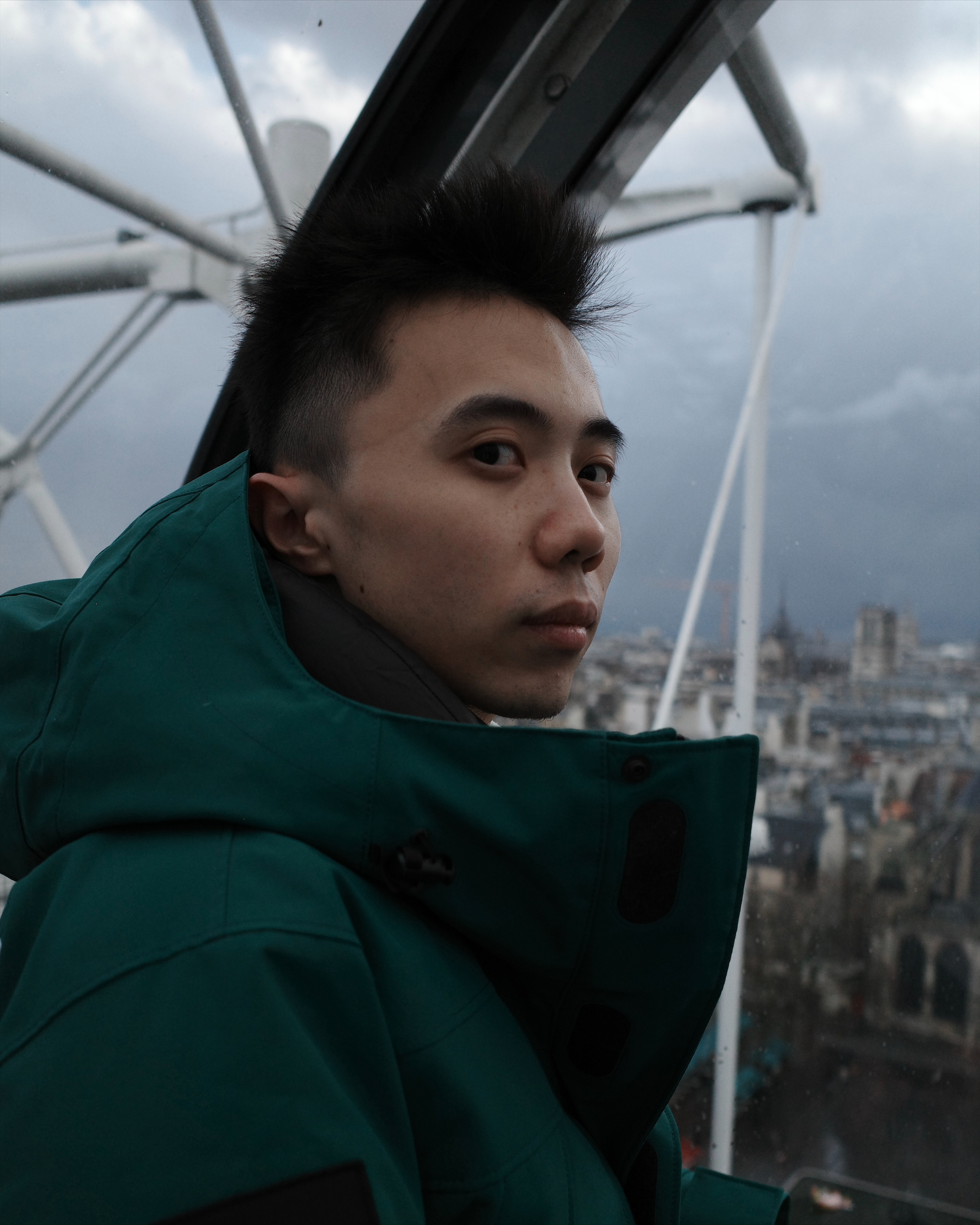 An Asian man in a jacket looks towards the camera against a backdrop of a distant city