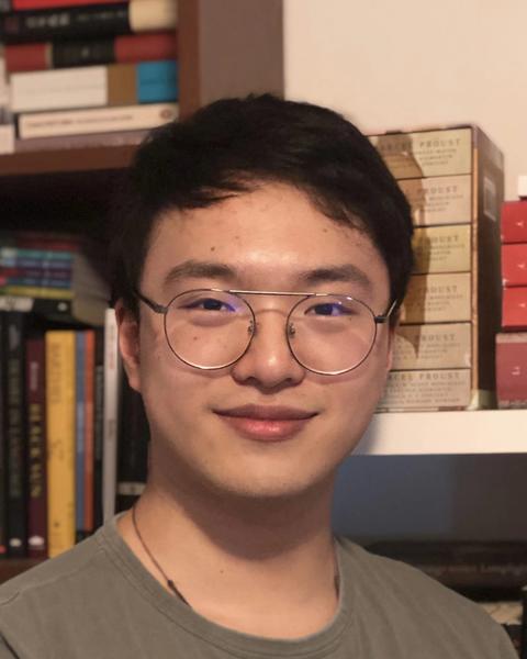 A Chinese man with round glasses smiles at the camera